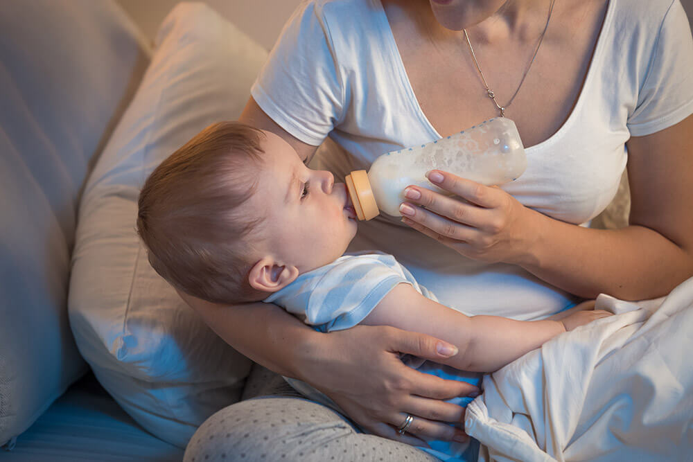 bedtime routines blog post image; sleepy baby drinking a bottle while being held by mom